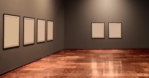 Une salle d'exposition aux murs gris, avec des cadres encore vides